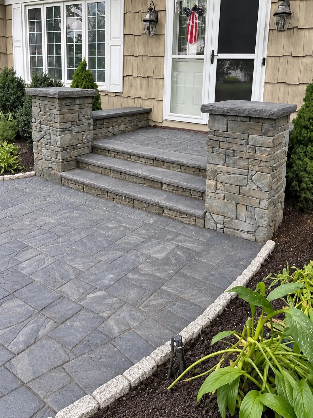Close view of stone entrance steps, masonry piers, paver landing, and garden bed