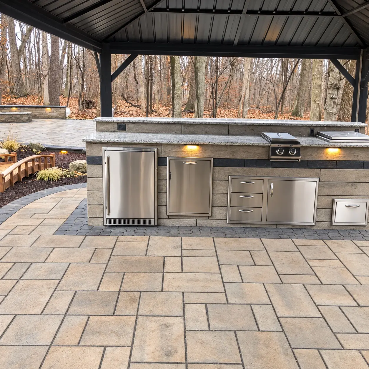 Built-in outdoor kitchen with stainless-steel appliances, stonework, and paver flooring