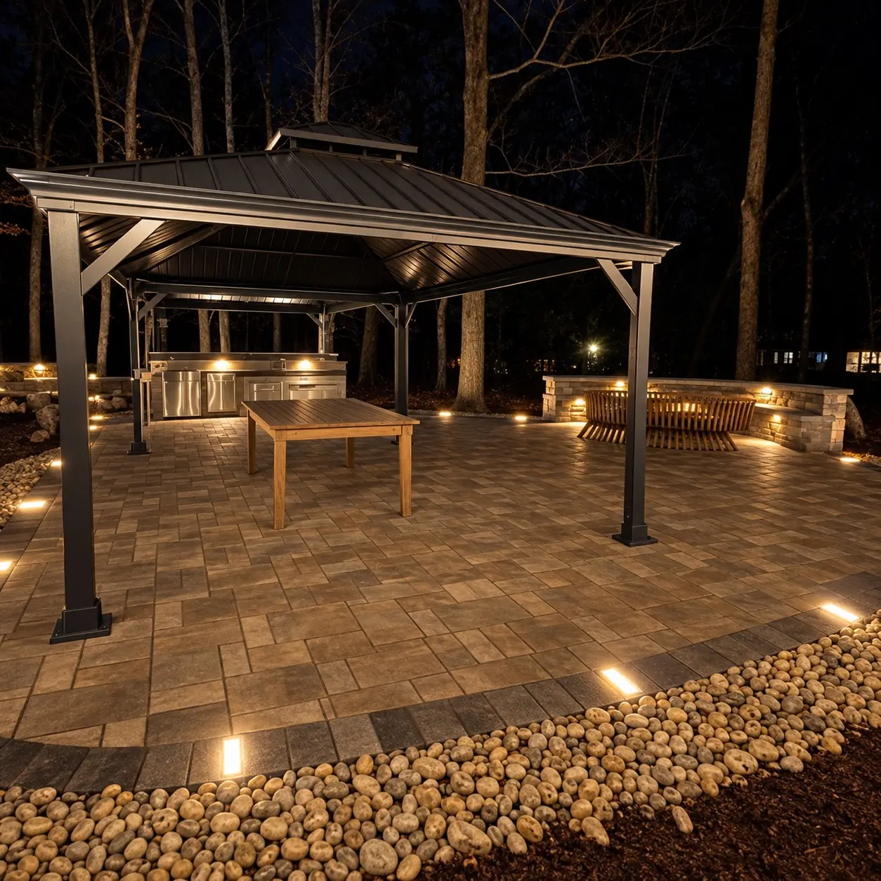 Outdoor pavilion, kitchen, paver patio, and seating wall illuminated at night