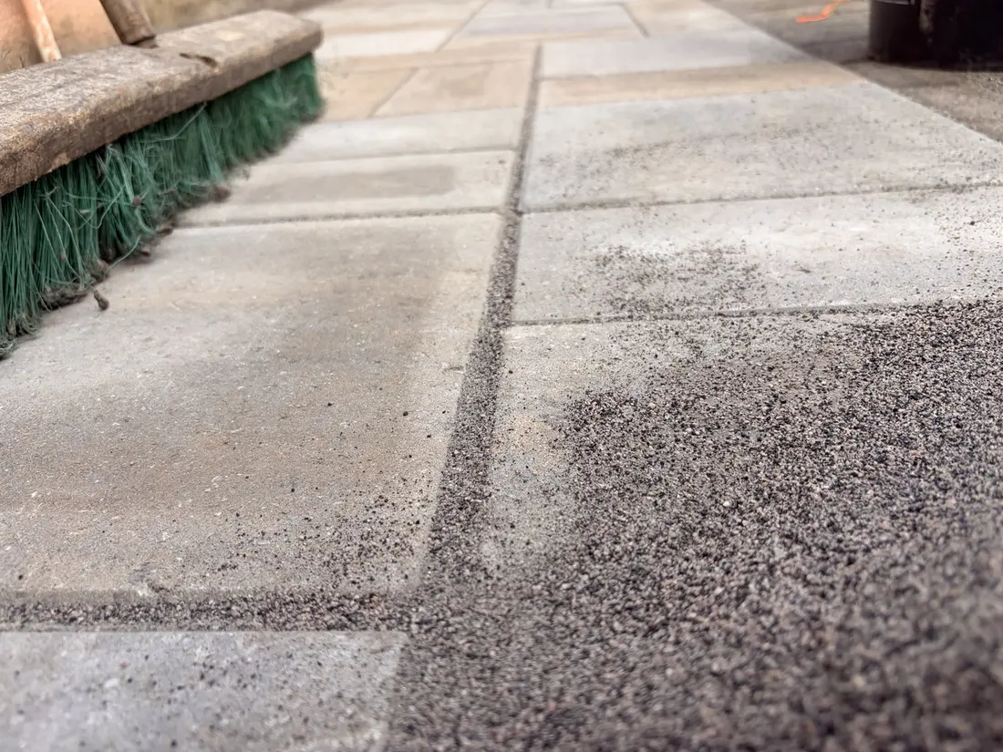 Joint material being carefully swept across installed patio pavers